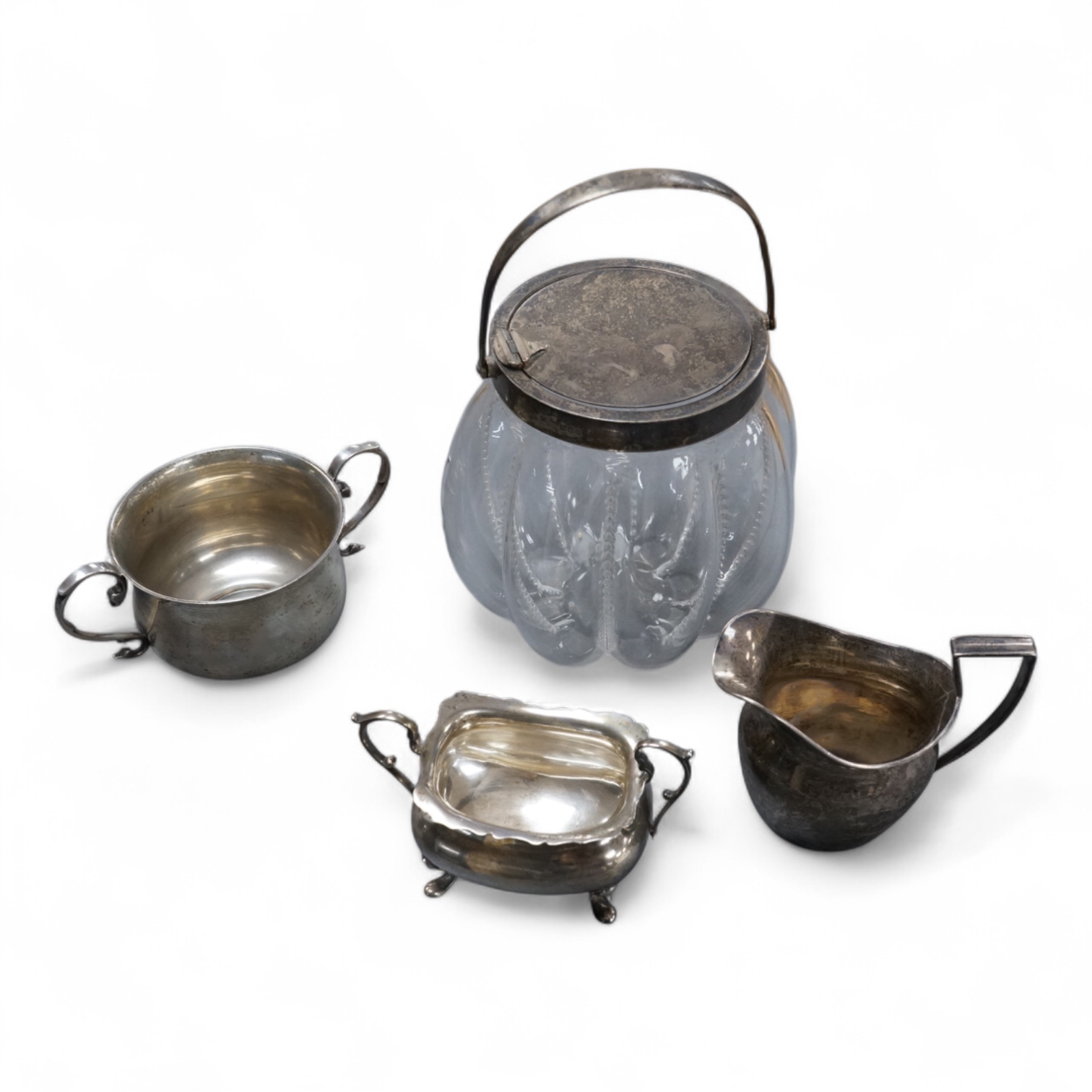 A late Victorian silver mounted lobed glass biscuit barrel by Hukin & Heath, with patent handle, London, 1899, height 14.4cm excluding the handle, together with a silver two handled condiment, a silver sugar bowl and a s